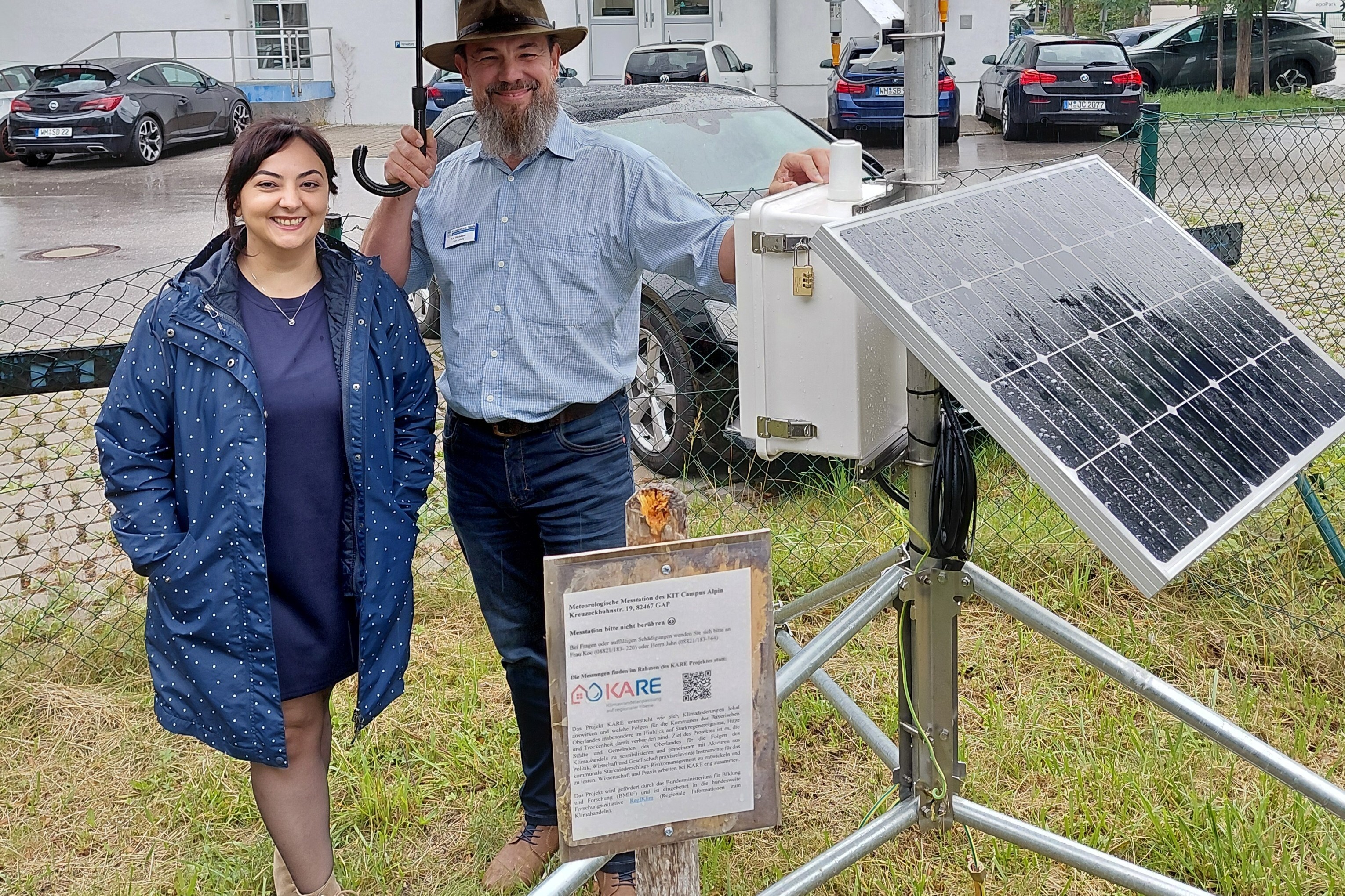 Zwei Personen stehen neben einer Solaranlage mit Infotafel und KARE-Logo.